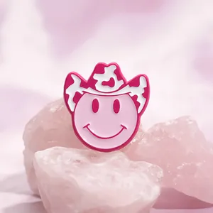 Detail of pink smiley enamel pin wearing a cow print cowboy hat on pink crystal