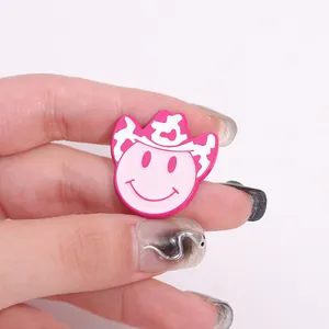 Detailed close-up of a pink smiley face pin with a cow print cowboy hat held in hand