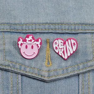 Detail view of pink cowboy hat and Be Kind heart enamel pins on denim jacket