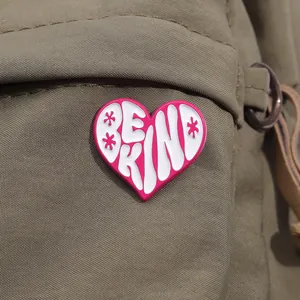 Close-up of a pink heart enamel pin with Be Kind text on a khaki canvas bag