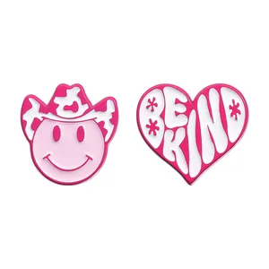 Pink enamel pin set with smiling face in cowboy hat and Be Kind heart design