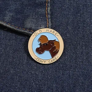 Macro detail of 'OLD MARE DON'T CARE' enamel pin badge pinned on blue denim fabric