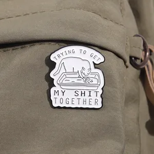 Détail du pin's chat blanc en émail sur un sac vert avec texte humoristique et design créatif