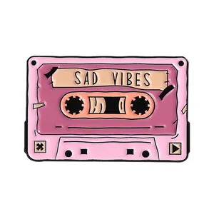 Detail of retro cassette enamel pin featuring SAD VIBES text in pink and purple colors