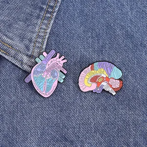 Enamel heart and brain organ pins with anatomical labels on blue denim fabric