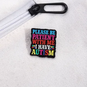 Close-up of autism awareness enamel pin with 'Please Be Patient With Me' text on white bag