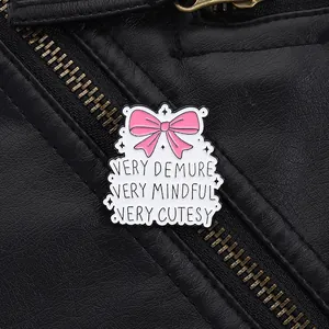 Detail of enamel pin with pink bow and Very Demure Very Mindful text on black leather