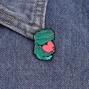 Nahaufnahme einer grünen Emaille-Dinosaurier-Brosche mit Herz auf blauem Denim