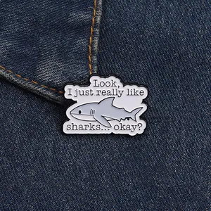 Detail of shark enamel pin with funny quote on dark blue denim fabric background