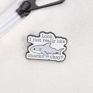 Detail of cartoon shark enamel pin with 'I just really like sharks' quote on canvas bag