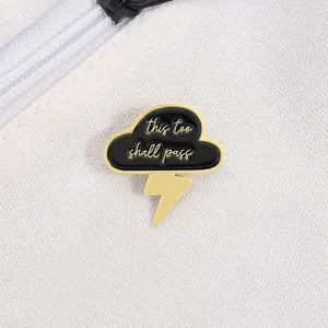 Detail of enamel cloud pin with gold lightning and text this too shall pass on canvas