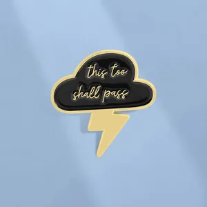 Minimalist black cloud and golden lightning enamel pin with 'this too shall pass' quote