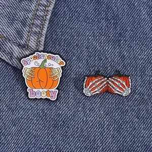 Close-up of Halloween enamel pins with skeleton hand and pumpkin on denim fabric
