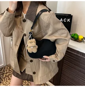 Detail of black leather hobo bag with a plush bear charm worn with a trench coat