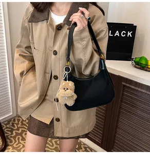 Detail of black crescent hobo bag with gold zipper and a cute beige puppy plush pendant