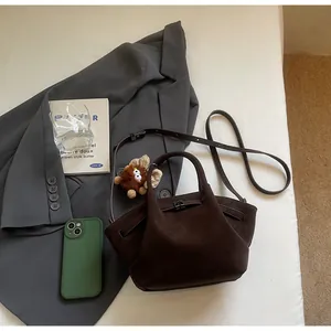 Nahaufnahme der braunen Wildleder-Beuteltasche mit Metallschnalle und Plüsch-Anhänger