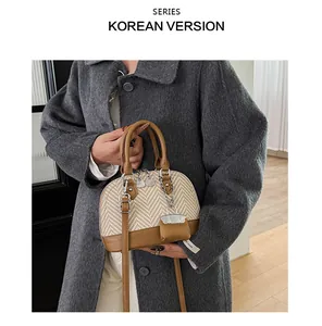 Close-up of a woven shell-shaped handbag with brown leather handles and gold chain charms
