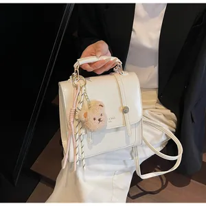 Detail of cream white leather crossbody bag with teddy bear charm and strap handle