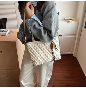 Detail of white woven textured handbag with wooden bead charm and long shoulder strap