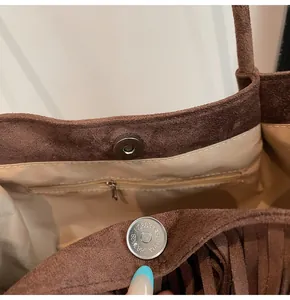 Detail of brown suede tote bag featuring a magnetic snap closure and tassel decoration