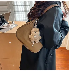 Brown suede hobo bag with plush puppy charm worn by model over a black leather jacket