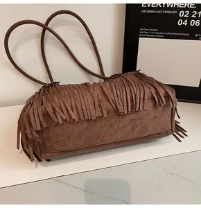 Detailed close-up of dark brown suede fringe tote bag on white marble surface