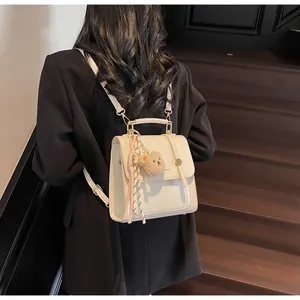 Detail view of cream white PU leather backpack with teddy charm and silk ribbon on model