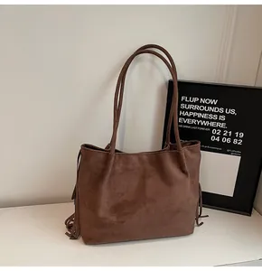 Detail of a dark brown suede tote bag featuring long side tassels and long handles