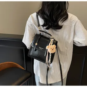 Detail of black glossy PU leather crossbody bag with teddy bear pendant and metal rivets