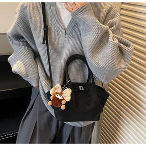 Detail der schwarzen Wildleder-Tasche mit Silberschloss und Plüschtier auf Strickpullover