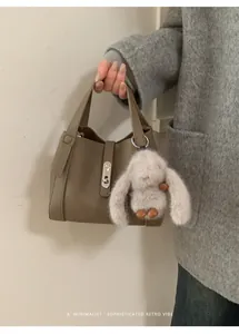 Detail of taupe lychee leather handbag with plush bunny charm and silver metal lock