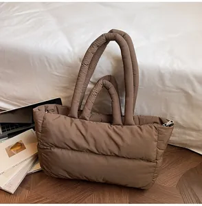 Close-up of dark brown quilted puffer tote bag with silver zipper on wood floor