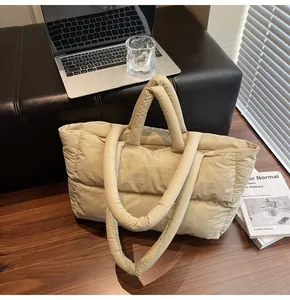 Detail of beige quilted puffer tote bag on wooden desk showing texture and dual handles