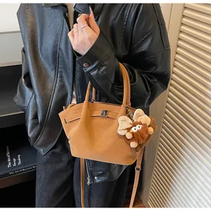 Detail der karamellfarbenen Wildleder-Tasche mit Plüsch-Anhänger und Metallschnalle