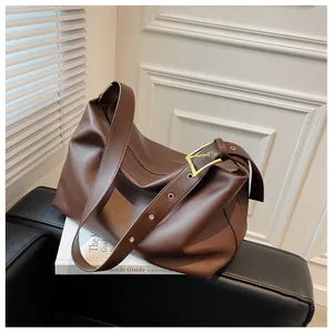 Detail of a brown leather hobo bag with a prominent gold square buckle and textured finish
