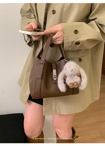 Detail of dark brown leather tote with silver lock and grey plush rabbit pendant