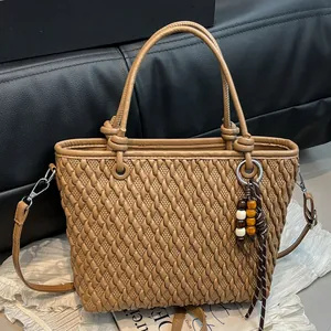 Brown woven crossbody bag with cylindrical handles and bead tassel on textured background