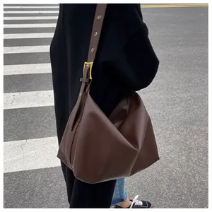Close-up of dark brown leather tote bag with wide shoulder strap and gold buckle detail