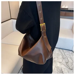 Detail of a brown leather shoulder bag featuring a wide strap with gold eyelets and buckle