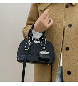 Detail of black shell-shaped crossbody bag featuring woven texture and heart charm