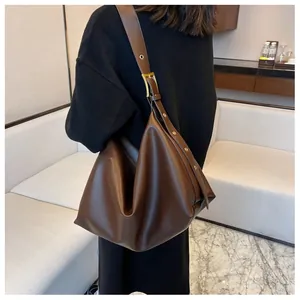 Detail of soft dark brown leather hobo bag featuring wide strap with gold metal eyelets
