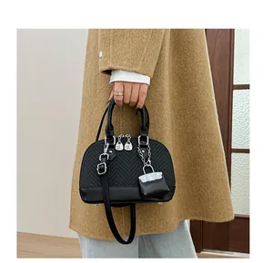 Detail of black shell bag with twill texture and mini charm worn on a camel coat
