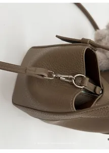 Detail of brown textured leather bag with silver hooks and a grey faux fur pompom charm