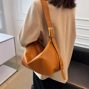 Minimalist orange-brown leather hobo bag with gold buckle shown on a model