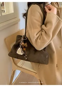 Détail d'un cabas en daim marron foncé avec breloque cœur et pompon sur le mannequin