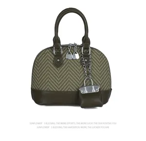 Detail of dark green shell bag with straw weave texture, twin handles and mini bag charm