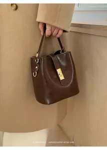 Close-up of brown leather bucket bag with gold clasp held by a model in a wool coat