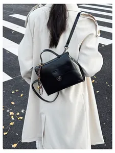 Vintage Umhängetasche aus schwarzem Leder mit Schleifenanhänger auf einem beigen Trenchcoat