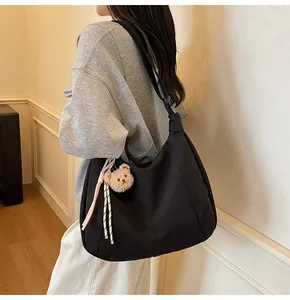 Détail d'un grand sac hobo noir avec un porte-clé ours en peluche et décor de corde