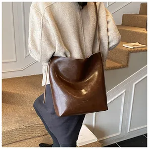 Detail of a large brown vintage oil wax leather bucket bag worn with a beige fleece coat
